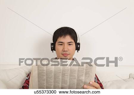 Stock Image - Man listening to music and reading the newspaper. Fotosearch