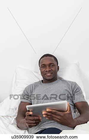 Stock Photo - Man looking at camera and holding his tablet. Fotosearch