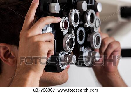 Stock Photo - Man looking through the keratometer. Fotosearch