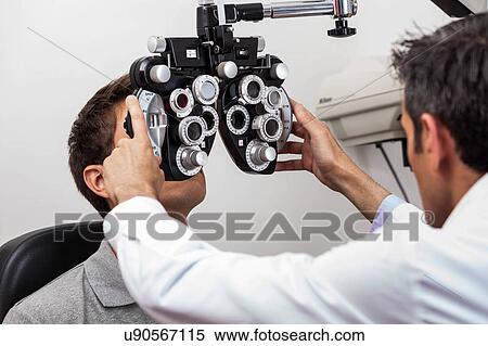 Stock Photography - Man looking through the keratometer. Fotosearch