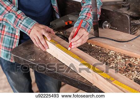 Stock Image - Man measuring a piece of wood. Fotosearch