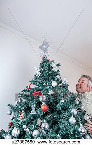 Stock Image - Man placing the star on the christmas tree . Fotosearch