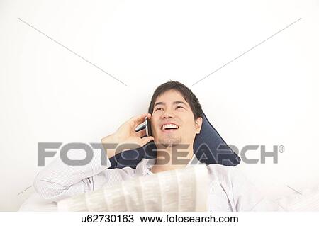 Stock Image - Man reading the newspaper and talking by phone. Fotosearch