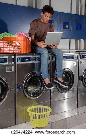 Picture - Man sitting on top of the washing machine. Fotosearch