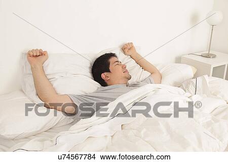 Picture - Man stretching in his bed. Fotosearch