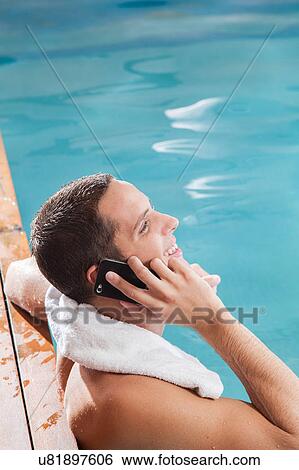 Stock Photograph - Man use the cellphone in the edge of the pool. Fotosearch