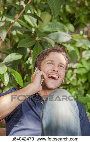 Stock Image - Man using a cellphone in the park. Fotosearch