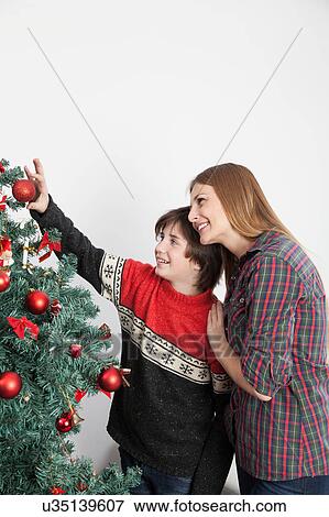 Mom with her son putting ornaments on the christmas tree View Large Photo Image Stock Photo - Mom with her son putting ornaments on the christmas tree. Fotosearch