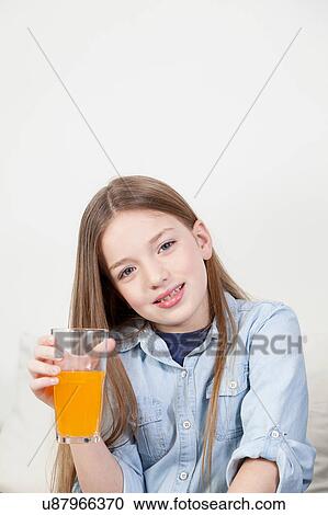 Stock Image - Pretty girl holding a glass with orange juice. Fotosearch