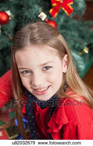 Stock Photo - Pretty girl sitting beside the christmas tree. Fotosearch