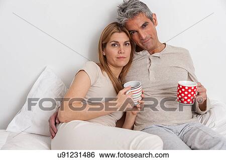 Stock Photograph - Serious couple drinking coffe in the bed. Fotosearch