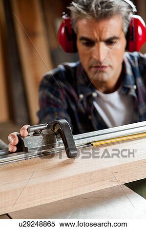 Stock Photography - Serious man measuring a piece of wood. Fotosearch