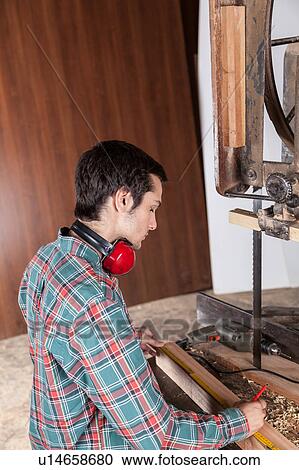 Stock Image - Serious man measuring piece of wood. Fotosearch