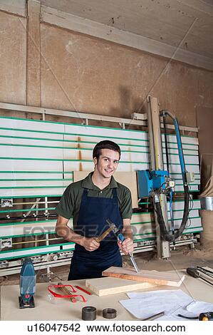 Stock Image - Smiling carpenter working with a chisel. Fotosearch