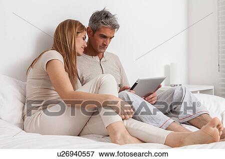 Stock Photo - Smiling couple in the bed using the ipad. Fotosearch