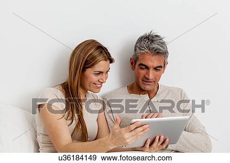 Smiling couple using the ipad View Large Photo Image Stock Photo - Smiling couple using the ipad. Fotosearch