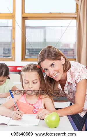 Stock Photo - teacher helping a girl in the classroom. Fotosearch