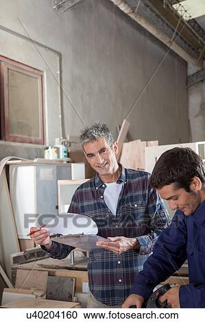 Stock Image - The carpenter supervising his assistant. Fotosearch