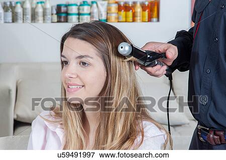 Stock Photo - The coiffeur use a curling iron. Fotosearch