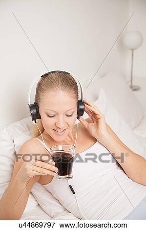 Stock Photo - Young woman listening to music and drinking coffe. Fotosearch