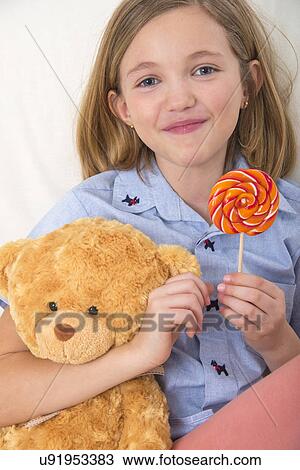 Stock Image - Girl holding a lollypop and teddy bear.. Fotosearch