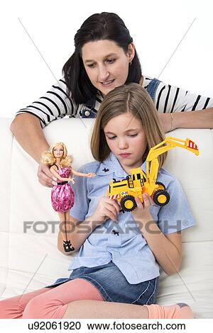 Stock Image - Girl playing with a toy truck and mother holding a doll.. Fotosearch