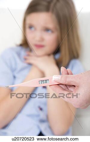 Stock Image - Person holding a digital thermometer with a girl in the background.. Fotosearch
