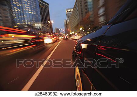 Stock Image - Car driving through city at dusk. Fotosearch
