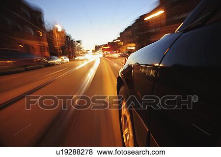 Stock Photo - Car driving through city at dusk. Fotosearch
