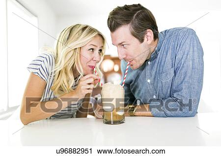 Stock Image - Couple drinking beer from drinking straw. Fotosearch
