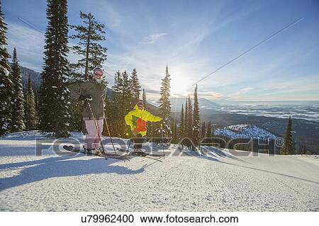 Stock Image - Couple standing on ski slope at sunlight. Fotosearch