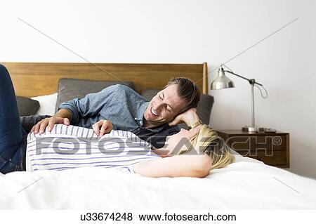 Stock Photo - Husband lying down on bed with pregnant wife. Fotosearch