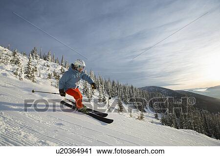 Stock Image - Mature man on ski slope at sunset. Fotosearch
