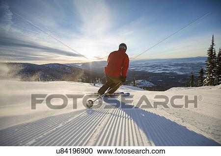 Stock Image - Mature man on ski slope at sunset. Fotosearch