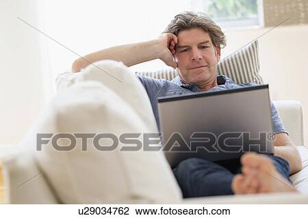 Mature man using laptop on sofa View Large Photo Image Stock Image - Mature man using laptop on sofa. Fotosearch
