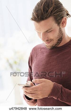 Stock Photo - Mid-adult man texting indoors. Fotosearch