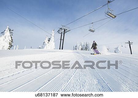 Stock Photo - Mid-adult woman on ski slope under cable car. Fotosearch