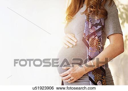 Stock Photograph - Mid-section of pregnant woman outdoors. Fotosearch
