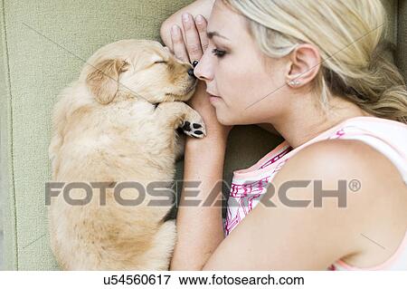 Stock Photo - Portrait of puppy with owner lying down on sofa. Fotosearch