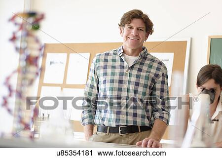 Stock Image - Portrait of teacher indoors, girl (10-11) using microscope in background. Fotosearch