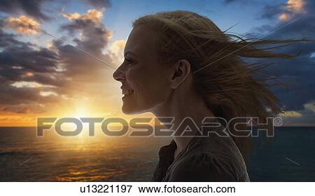 Stock Photo - Portrait of woman by sea at sunset. Fotosearch