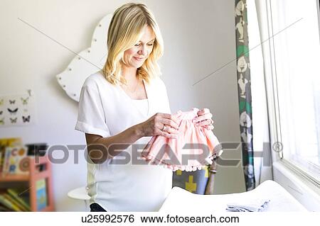 Stock Photograph - Pregnant woman holding baby clothing. Fotosearch