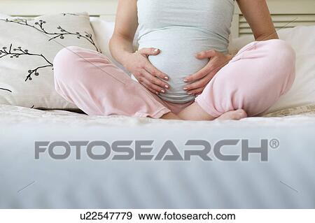 Stock Photo - Pregnant woman sitting on bed. Fotosearch