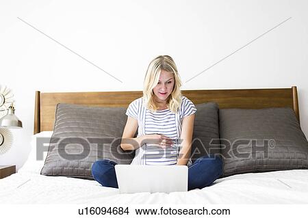Picture - Pregnant woman using laptop in bed. Fotosearch