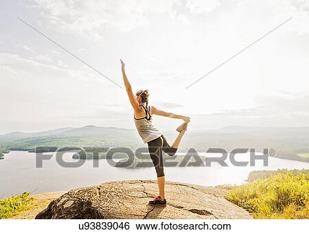 Stock Photograph - Side view of young woman exercising on mountain top. Fotosearch