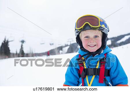 Stock Image - Smiley little boy (5) wearing ski suit in mountains. Fotosearch