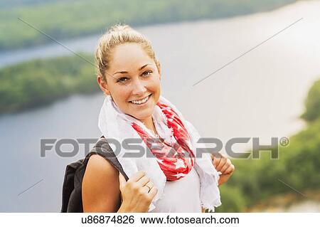 Stock Photograph - Smiley young woman against lake view. Fotosearch
