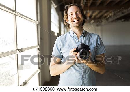 Stock Image - Smiling man with digital camera. Fotosearch