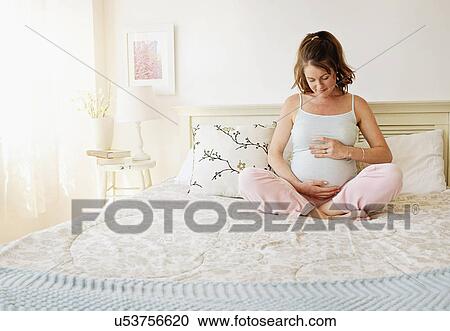 Smiling pregnant woman sitting on bed View Large Photo Image Stock Image - Smiling pregnant woman sitting on bed. Fotosearch