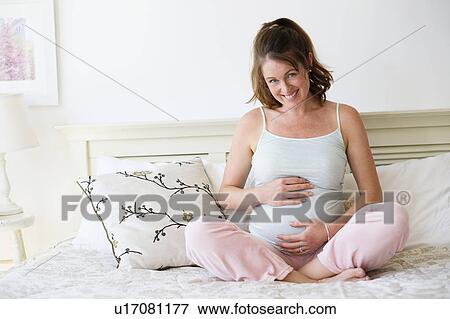 Smiling pregnant woman sitting on bed View Large Photo Image Stock Photo - Smiling pregnant woman sitting on bed. Fotosearch